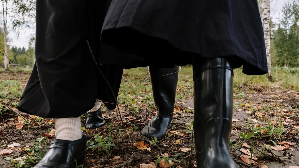 Close-up of people walking in a forest wearing rubber boots, amidst fallen autumn leaves.